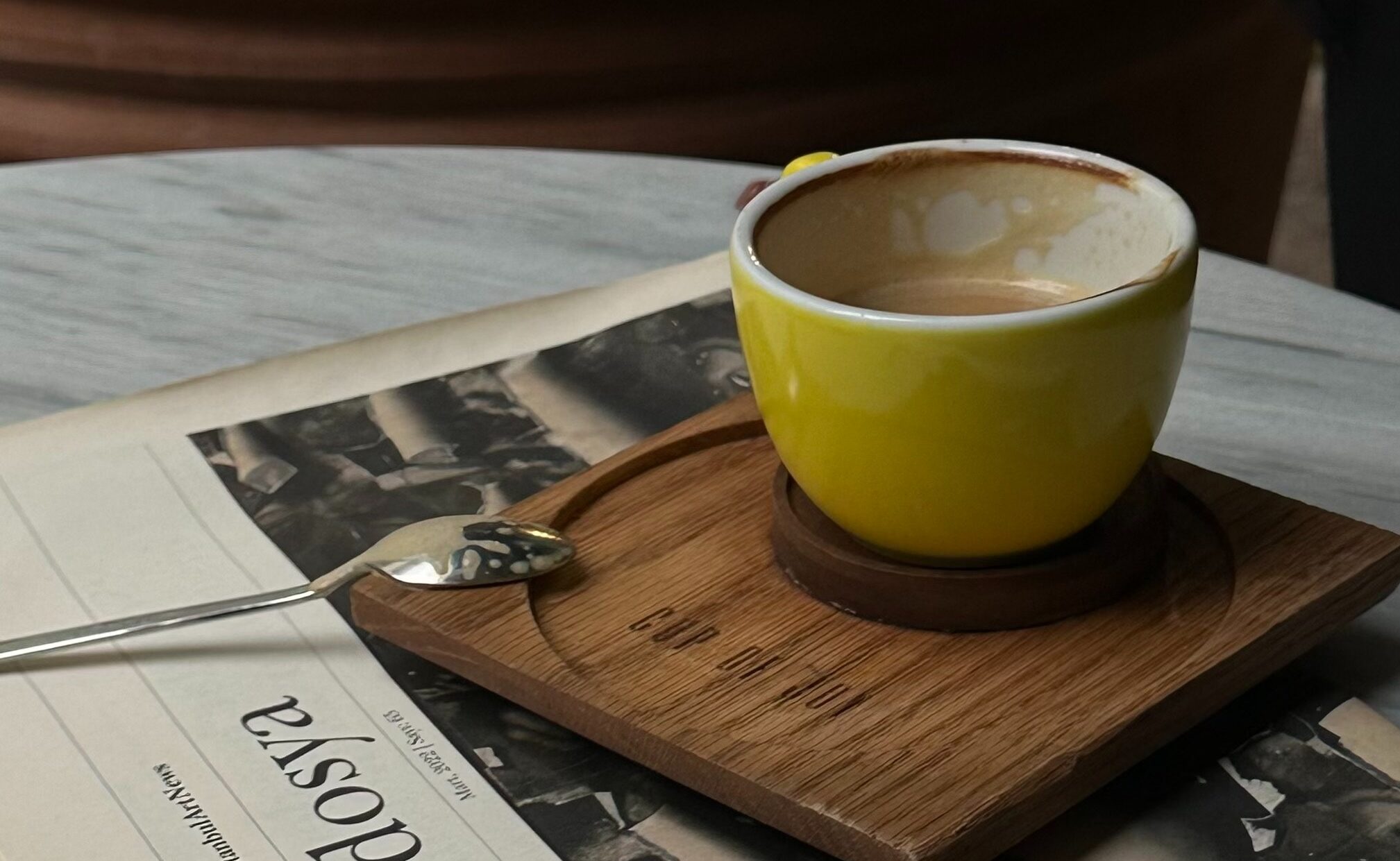 Photograph of half empty coffee cup and used spoon sitting on top of a newspaper.