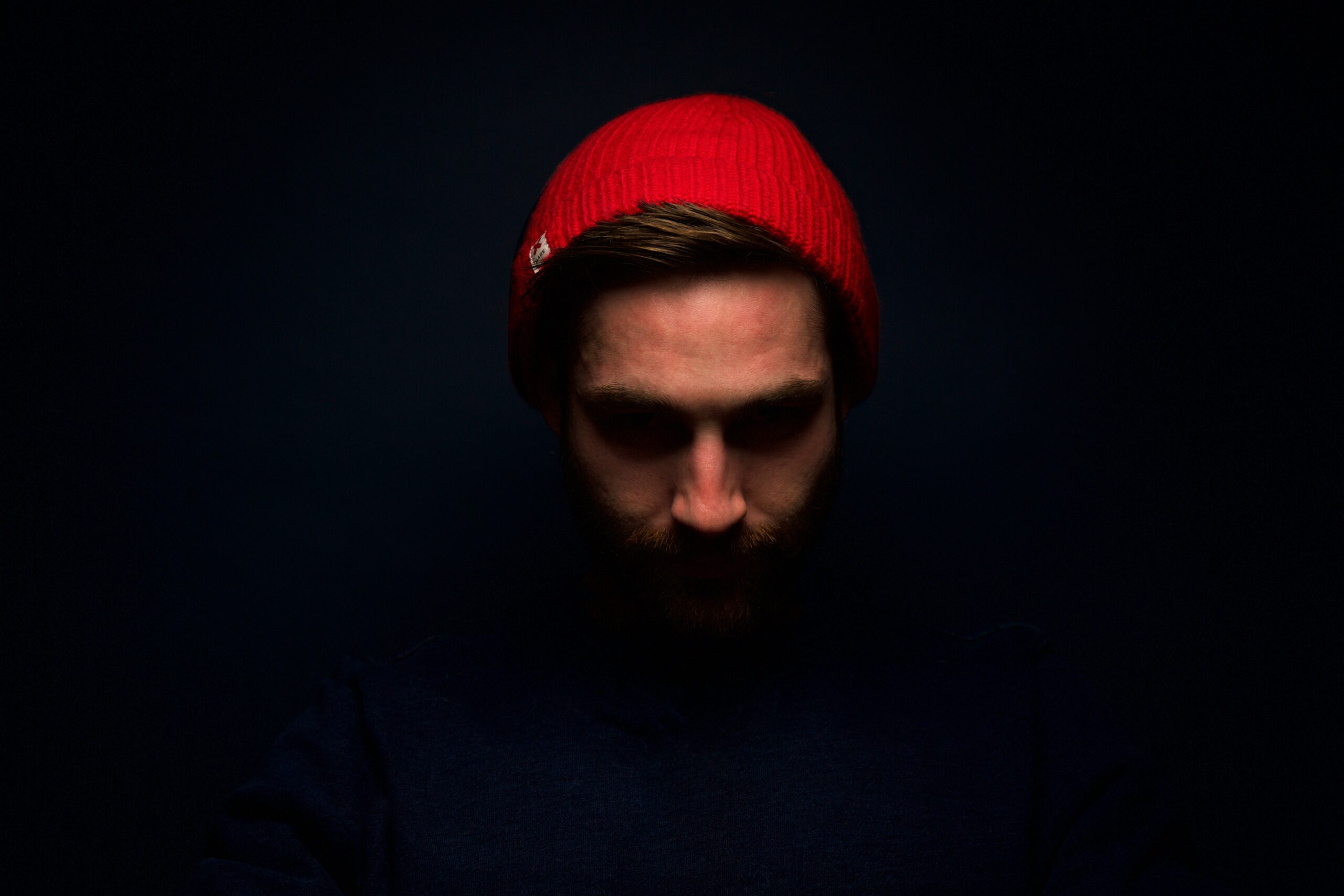 A photograph of a caucasian man wearing red knit cap in dark room
