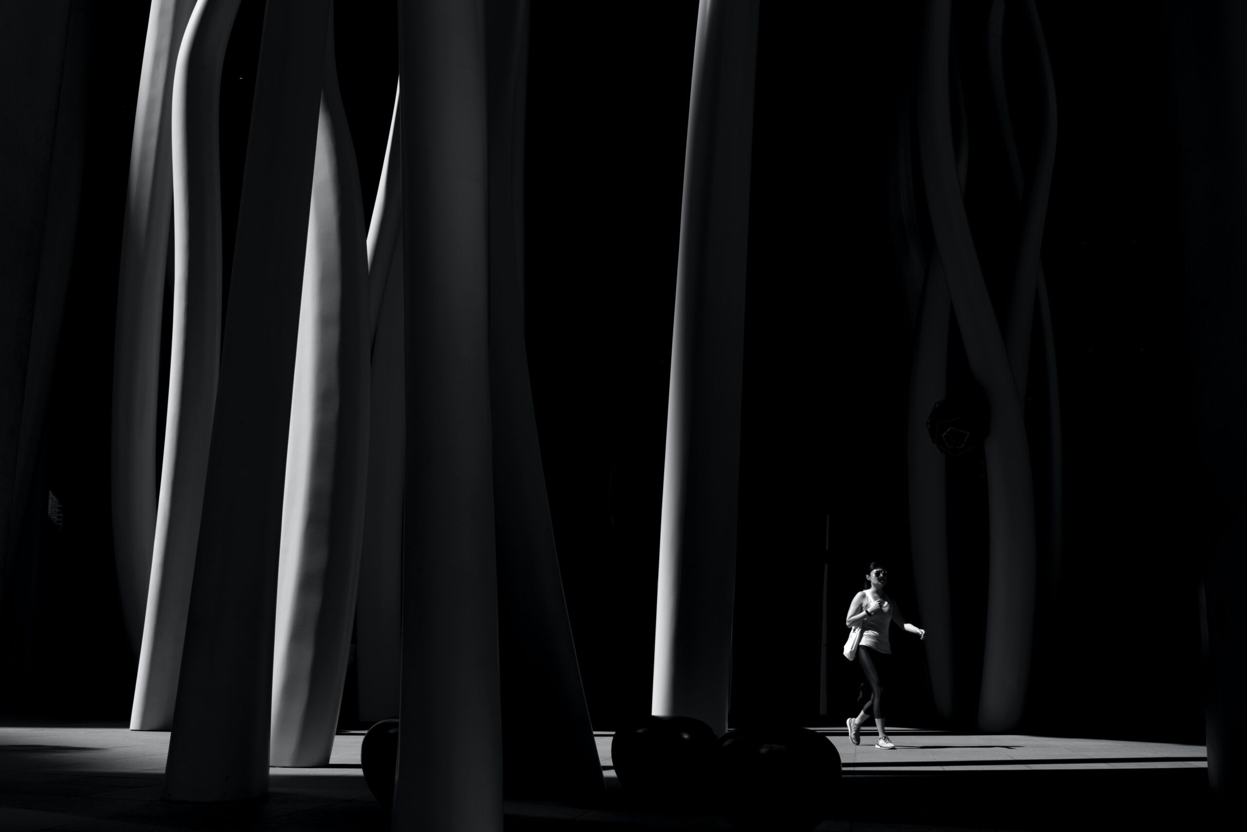 Grayscale Photo of Person Wearing Black Pants Walking Across Posts.